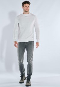 Hellgrauer, gerippter Strickpullover mit Rundhalsausschnitt, kombiniert mit grauer Jeans und dunklen Stiefeln, mit entspannter Passform und dezentem Markendetail.