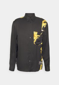 Zwarte shirt met lange mouwen en een geel barokpatroon aan de linkerkant en op de zak. Gemaakt van gladde stof, met een knoopsluiting aan de voorkant.