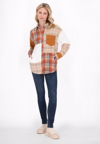 Rutig skjorta i nyanser av orange, beige och vitt, med en kordflugan ficka, långa ärmar och knäppning framtill. Bärs med mörka jeans.