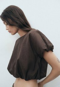 Brauner cropped Top mit puffärmeln und rundem Ausschnitt. Weicher, glatter Stoff mit lockerer, entspannter Passform und gerafftem Saum.