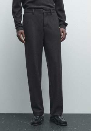 Pantaloni in lana grigia scura con un design a gamba dritta, dotati di un unico bottone frontale e tasche laterali, abbinati a mocassini neri.