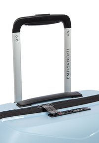 Světle modrý tvrdý kufr s texturovaným povrchem, černým zipovým uzávěrem a hliníkovou teleskopickou rukojetí. Obsahuje logo "EMILY & NOAH."