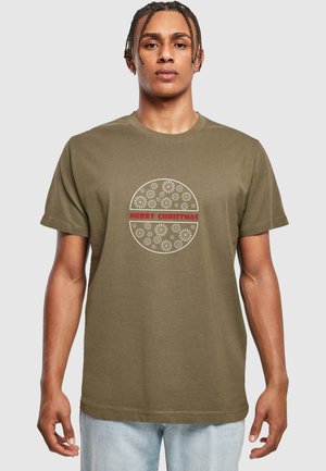 Tricou din bumbac de culoare verde măslin, având un design grafic rotund cu motive florale albe și textul roșu "CRĂCIUN FERICIT" în centrul acestuia.