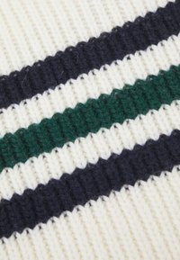 Strikket stoff med vekslende striper av krem, mørk marineblå og grønn. Teksturen er tykk, ribbet og myk, med dybde som fremheves.