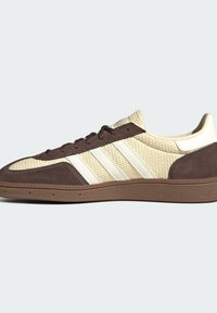 Χαμηλά sneakers από μπεζ υφασμάτινο με υφή, καφέ επενδύσεις από σουέτ, λευκές ρίγες στα πλευρά, καφέ κορδόνια και καφέ ελαστική σόλα.