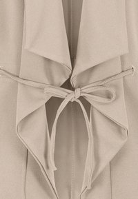 Cardigan beige à effet drapé, avec fermeture à nouer à la taille et tissu doux et texturé. Pas de motifs ni de détails métalliques visibles.