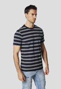 T-shirt rayé marine avec des rayures blanches horizontales, col rond, manches courtes, et un petit logo sur la poitrine ; fabriqué en tissu de coton doux.