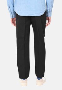 Pantaloni neri realizzati in un materiale liscio, con una vestibilità ampia e pieghe, abbinati a sneakers chiare e una camicia di jeans.