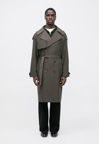 Dark gray trench coat with a double-breasted design, wide collars, and a waist tie, worn over a black knit top and trousers.