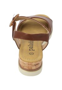 Brązowe skórzane sandały na paski z korkowym obcasem i wyściełaną jasnobezową wkładką. Posiadają okrągłą klamrę i jasną podeszwę.