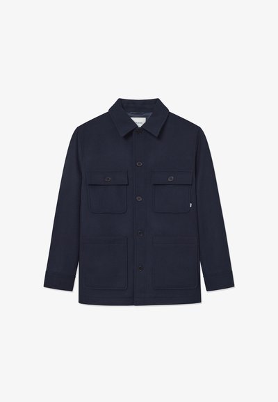 Casaco azul-marinho feito de um tecido robusto, com fecho de botão, gola ampla e dois grandes bolsos peitorais com fechos de aba.