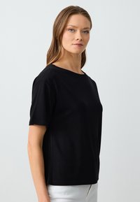 Zwarte T-shirt met korte mouwen en een ronde hals. Gemaakt van zachte stof, met een relaxte pasvorm en naadloze zijkanten voor minimale details.