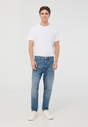 T-shirt bianco a maniche corte abbinato a jeans a gamba dritta azzurri e sneakers bianche, che mostrano un look casual e una classica texture denim.