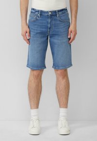 Shorts en denim bleu clair avec une coupe droite, ourlet roulé, cinq poches et fermeture à bouton métallique. Portés avec des baskets blanches et des chaussettes.