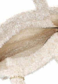 Interno della borsa beige peloso con texture morbida, dotato di chiusura con zip e un accento in catena dorata. Spaziosa con una fodera liscia.
