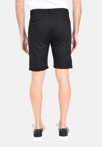 Pantaloni neri in tessuto con una texture liscia; presentano orli arrotolati, due tasche posteriori e una vestibilità attillata all'altezza del ginocchio.