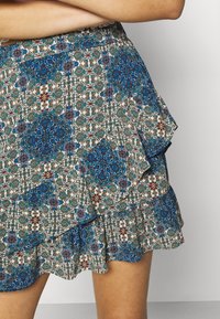 Jupe à volants à motif bleu, marron et blanc. Présente un imprimé décoratif floral et géométrique avec des détails à volants superposés.