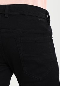 Svarta jeans i denim med en åtsittande design, bakficka med synlig sömnad och logotyp nära midjan.