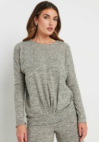 Maglia grigia a maniche lunghe realizzata in morbido tessuto a maglia, con scollatura rotonda e dettagli arricciati in vita per una silhouette rilassata.