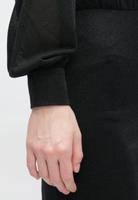 Černý top s dlouhým rukávem z texturované látky s třpytivým efektem. Nabírané rukávy se zužují u zápěstí a mají přiléhavý lem.