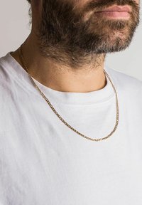 Guld kæde med led, der ligger på en hvid t-shirt. Kæden har en glat, skinnende overflade og et klassisk design.