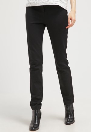 Pantalones negros ajustados hechos de una tela suave, con una cintura de altura media y piernas ajustadas, combinados con botas de tobillo brillantes en negro.