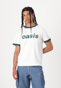 White cotton t-shirt with green ribbed collar and cuffs, featuring "oasis" in large green text on the front. Casual design.