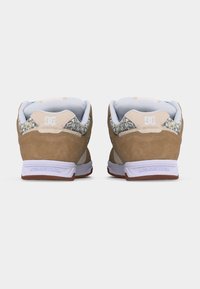 Ζευγάρι καφέ σουέντ αθλητικά παπούτσια DC με λεπτομέρειες σε σχέδιο λεοπάρδαλη και λευκές σόλες, εμφανιζόμενα από πίσω σε απλό λευκό φόντο.