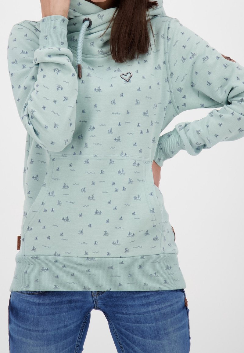 Sudadera verde claro con cuello alto, que presenta un estampado náutico de pequeños barcos y olas. Puños y dobladillo acanalados, con un detalle de corazón.