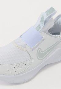 Chaussure de sport blanche avec tige en mesh, sangle élastique et bout arrondi. Présente un logo subtil et des perforations pour la respirabilité.