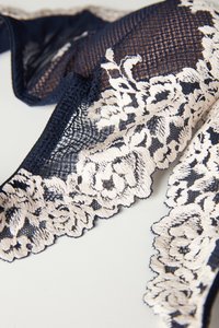 Námořnická krajka s vyšívaným květinovým vzorem v béžové barvě. Vyznačuje se jemnou síťovanou texturou a vroubkovanými okraji.