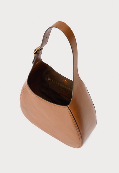 Καφέ δερμάτινη τσάντα ώμου με φαρδιά ρυθμιζόμενη τιράντα, επάνω άνοιγμα και εσωτερική τσέπη με φερμουάρ σε ανοιχτό φόντο.