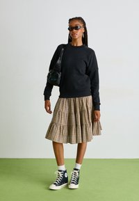 Felpa nera, gonna a balze a quadri nei toni del beige e marrone, sneakers alte navy, borsa nera piccola e occhiali da sole minimalisti.