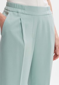 Pantalons texturés vert clair avec une taille élastique, poches latérales et plis à l'avant. Axé sur le confort et une coupe décontractée.