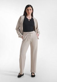 Beżowe spodnie dresowe z troczkami w połączeniu z dopasowanym czarnym topem z dekoltem w kształcie łezki, uzupełnione o pasującą beżową bluzę na zamek.