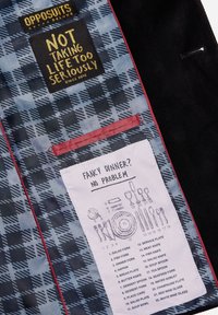 Kostymjackas insida med rutigt foder, lappar som säger "TA INTE LIVET FÖR SERIÖST," och en guide för middagsbestick märkt "FANCY DINNER? INGA PROBLEM."