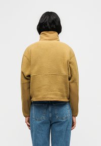 Φλις πουλόβερ σε μουσταρδί χρώμα με ψηλό γιακά, με υφή στο σώμα και λείες μανίκες. Συνδυάζεται με τζιν μεσαίου ύψους σε μπλε απόχρωση.