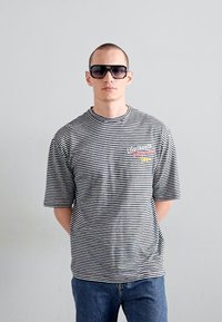 Un tricou cu mânecă scurtă în dungi alb-negru, cu guler rotund, care are accente grafice colorate, asortat cu blugi din denim bleu.
