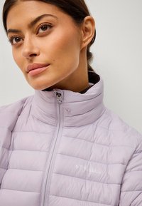 Giacca puffa viola chiaro con design trapuntato, colletto alto e zipper frontale. Presenta il logo sul petto, con una texture liscia e lucida.