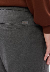 Grå bukser lavet af blødt, tekstureret stof med en påsyningslomme og et BOSS-logo mærke bagpå. Slim fit talje med elastik.
