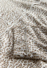 Leopardenmuster-Stoff in Beige- und Brauntönen mit Knopfverschluss, kontrastierender Paspelierung und weicher Textur.