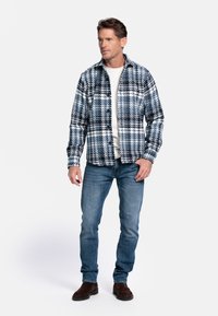 Geruite flanellen overhemd in blauw en witte tinten, met een knoopsluiting aan de voorkant en een spreidkraag. Gepaard met een lichtblauwe spijkerbroek en bruine laarzen.