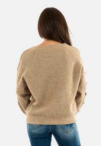 Maglione beige a coste con scollo ampio e maniche texturizzate, abbinato a jeans blu, visto da dietro su uno sfondo bianco.
