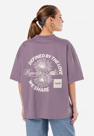 Fioletowy, oversize t-shirt wykonany z bawełny, z kwiatowym nadrukiem z tyłu oraz naszywką z logo z boku. Krótkie rękawy i okrągły dekolt.