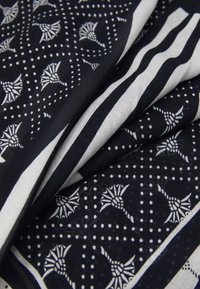 Schwarzer Stoff mit weißen Blumen- und Punktmustern, mit kontrastierenden gestreiften Rändern. Weiche Textur, in Falten drapiert.