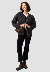 Chaqueta negra acolchada con botones en la parte delantera, combinada con pantalones de pana negros y botas de tobillo marrones. Sosteniendo un bolso de hombro marrón con estampado de leopardo.