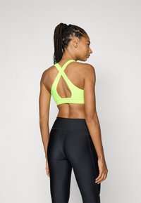 Neon grønn sports-bh med crossover ryggdesign, med en merket elastikk. Kombinert med høy-midje svarte leggings, med glatt tekstur.