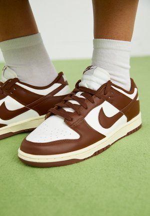 Baskets Nike marron et blanc avec lacets portées avec des chaussettes blanches sur un sol vert clair.