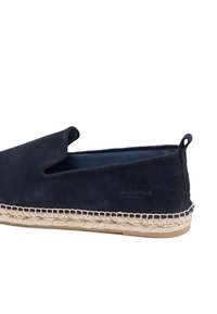 Chaussures à enfiler en suède bleu marine avec une semelle en corde de jute, présentant un design découpé et une finition texturée. Comprend un petit logo sur le côté.