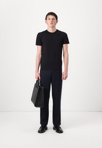 Juodas trumpas rankovėms marškinėliai, slim-fit mėlynos kelnės, juoda odinė rankinė su keliomis rankenomis ir juodi batai ant vientiso fono.